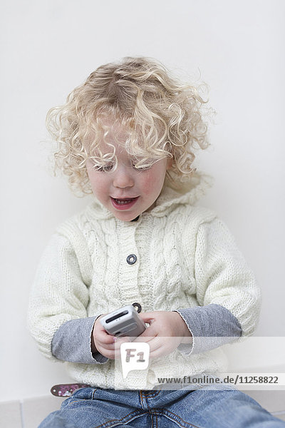 Porträt eines blonden Mädchens (4-5)  das mit einem Mobiltelefon spielt