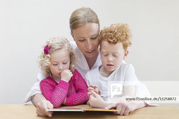 Mother reading book to son (8-9) and daughter (4-5)