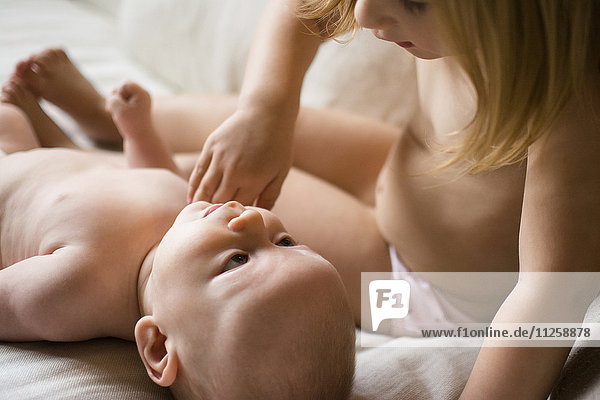 Girl (2-3) looking at baby brother (6-11 months) on bed