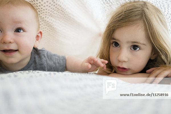 Mädchen (2-3) und kleiner Bruder (6-11 Monate) verstecken sich unter der Bettdecke