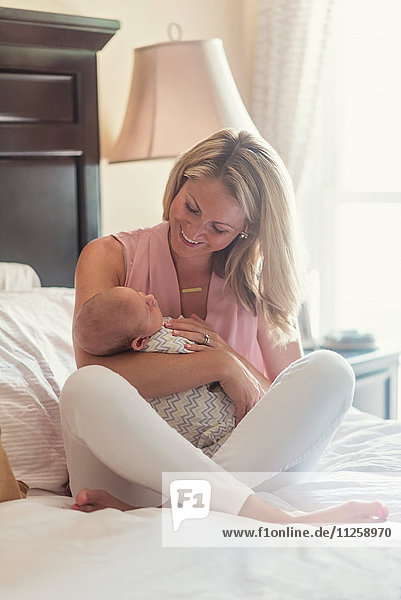 Mother sitting on bed and holding baby son (0-1 months)