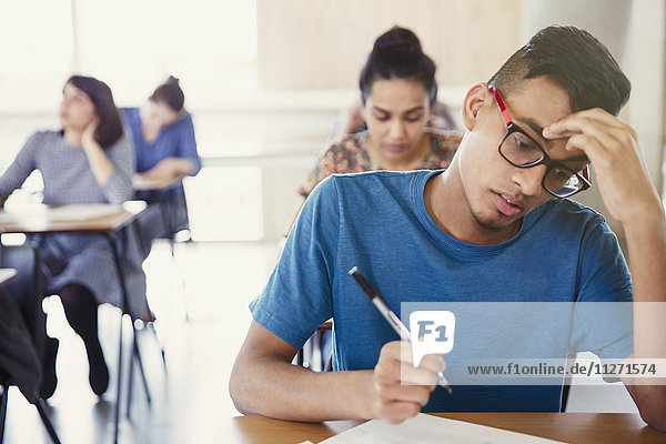 Serious male college student taking test at desk in classroom