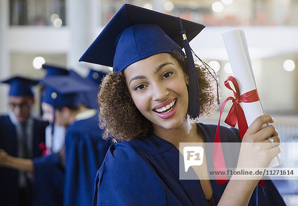 Portrait lächelnde Hochschulabsolventin in Mütze und Kleid mit Diplom