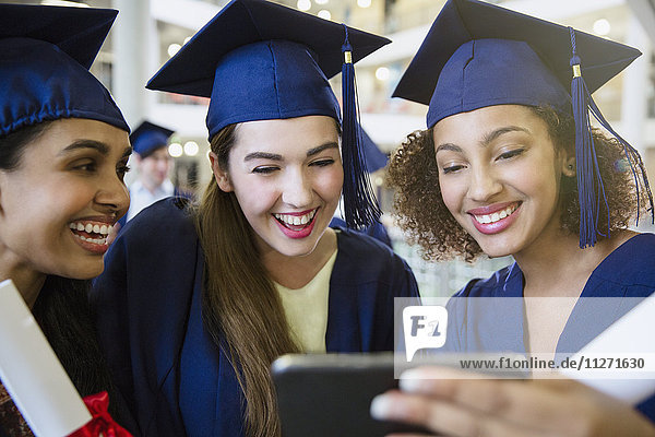 Smiling college graduates in cap and gown using cell phone