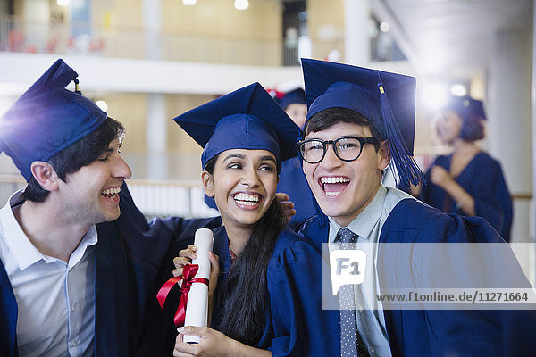 Glückliche Hochschulabsolventen in Mütze und Kleid feiern mit Diplom