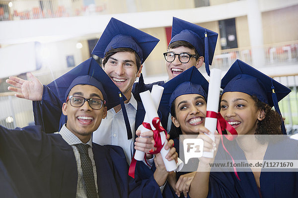 Glückliche Studenten in Mütze und Kleid mit Diplomen  die für Selfie posieren.
