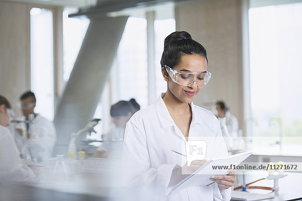 Female college student taking notes in science laboratory classroom