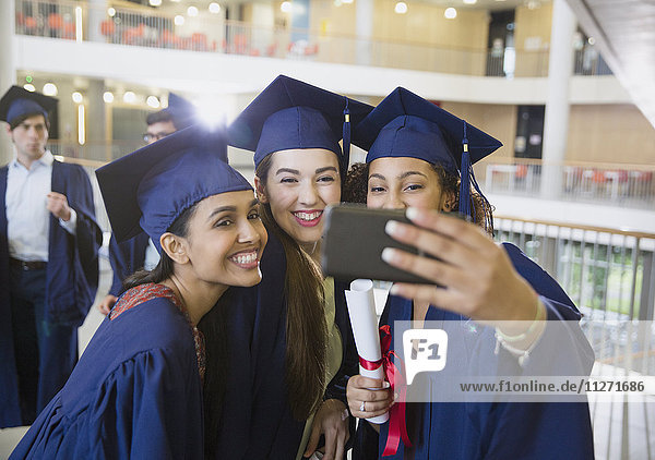 Female college graduates in cap and gown taking selfie