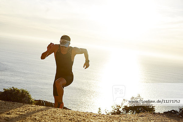 Male triathlete runner running uphill on sunny ocean trail