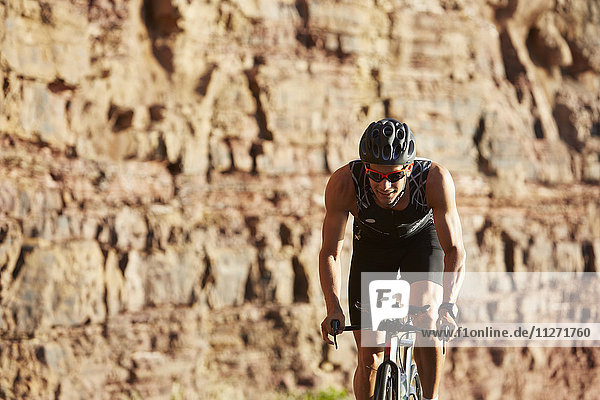 Male triathlete cyclist cycling along sunny rocks