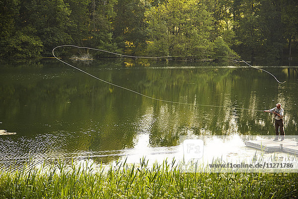 Senior man fly fishing on green summer lake