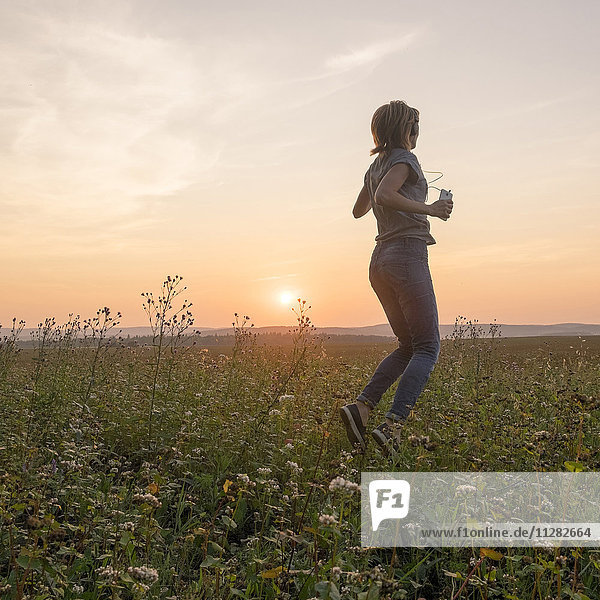 Caucasian woman dancing in field at sunset