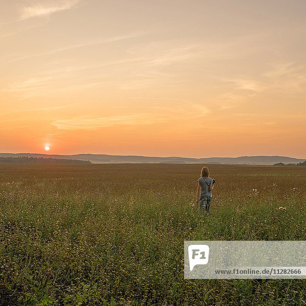 Kaukasische Frau  die bei Sonnenuntergang in einem Feld spazieren geht