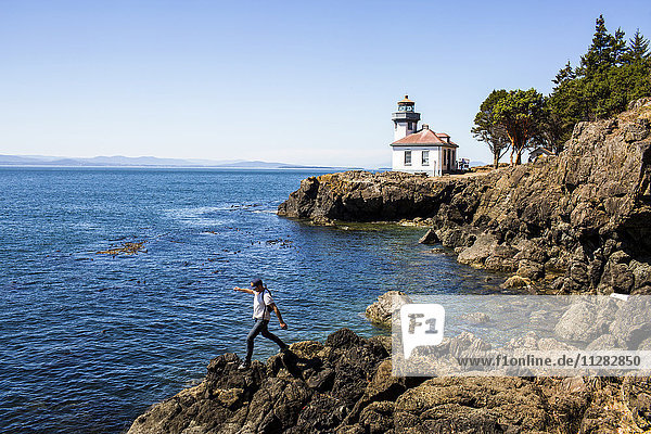 Caucasian man walking on rocks near lighthouse