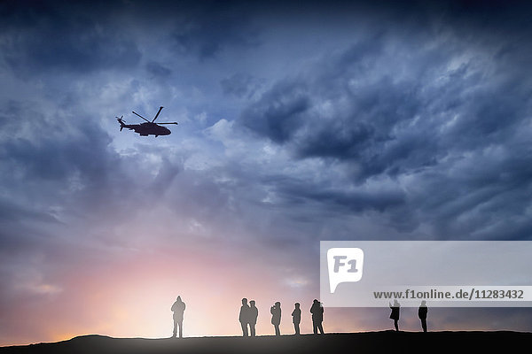 Silhouette eines Hubschraubers  der bei Sonnenuntergang über Menschen fliegt