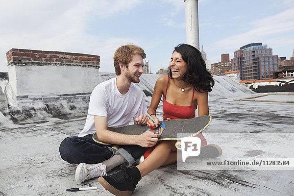 Mixed Race couple sitting on rooftop with skateboard