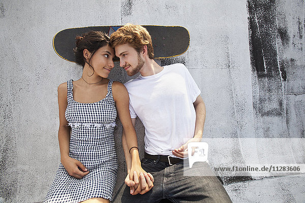 Gemischtrassiges Paar sitzt auf dem Dach mit Skateboard