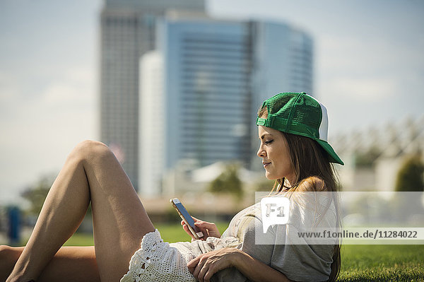 Kaukasische Frau liegt im Gras und schreibt eine SMS mit ihrem Handy
