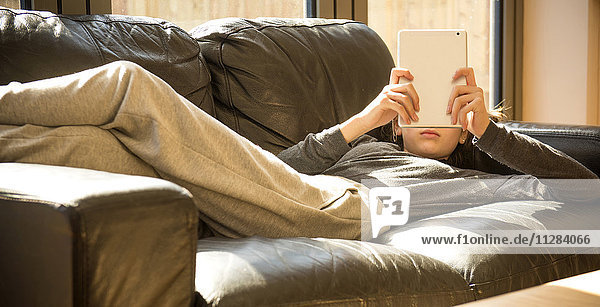 Girl laying on sofa reading digital tablet