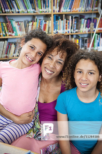 Lächelnde Mutter posiert mit Töchtern in der Bibliothek