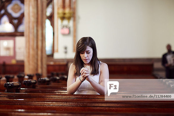 Kniende kaukasische Frau  die in einer Kirchenbank betet