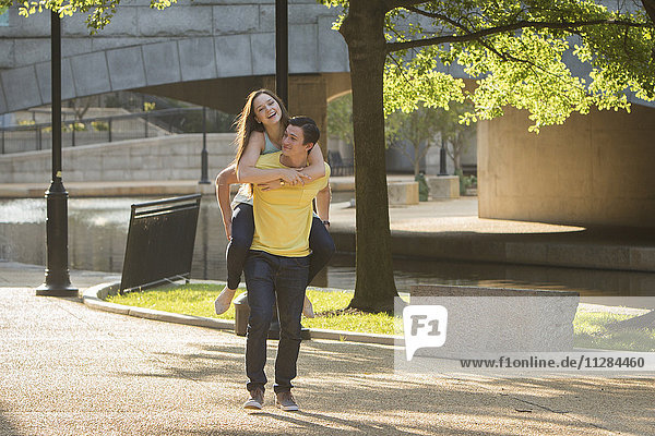 Caucasian man carrying girlfriend piggyback in park