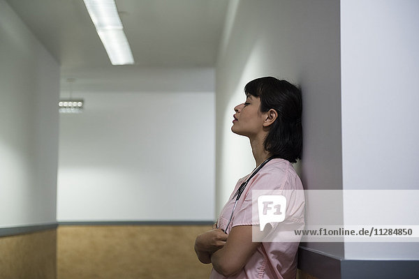 Müde hispanische Krankenschwester lehnt an der Wand im Krankenhausflur