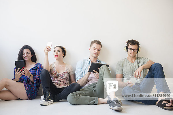 Caucasian friends sitting on floor using technology