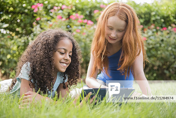 Smiling girls in grass field using digital tablet