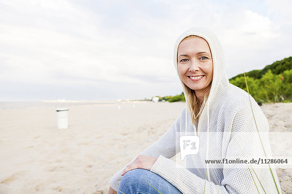 Frau mit Kapuzenshirt sitzt am Sandstrand