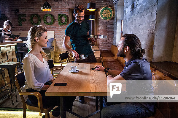Waiter serving espresso to couple in coffee shop