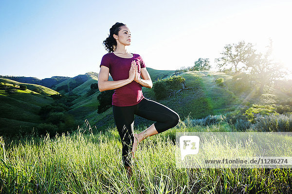 Mixed Race woman practicing yoga on hill