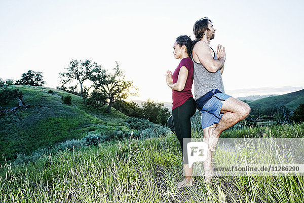 Couple practicing yoga on hill