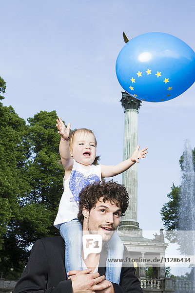 Girl on fathers shoulders catching balloon with European logo