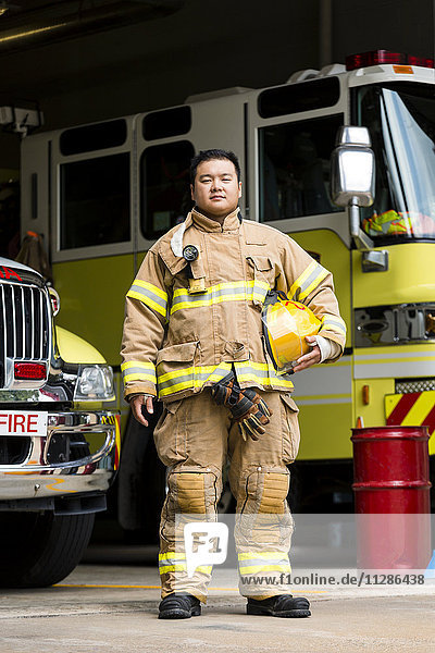 Ernster chinesischer Feuerwehrmann posiert in der Nähe von Feuerwehrautos