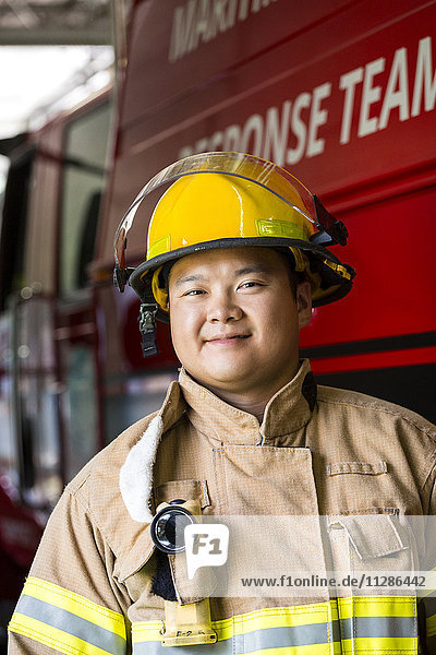 Lächelnder chinesischer Feuerwehrmann  der in der Nähe des Feuerwehrautos steht