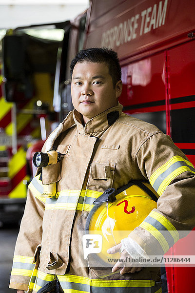 Ernster chinesischer Feuerwehrmann  der in der Nähe des Feuerwehrautos steht