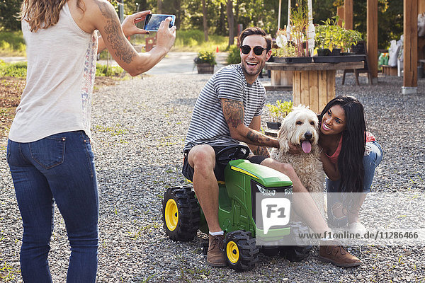 Frau fotografiert Paar und Hund mit Mobiltelefon
