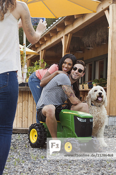Frau fotografiert Paar und Hund mit Mobiltelefon