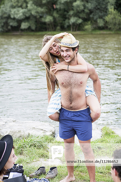 Young man giving girlfriend piggyback on the riverbank