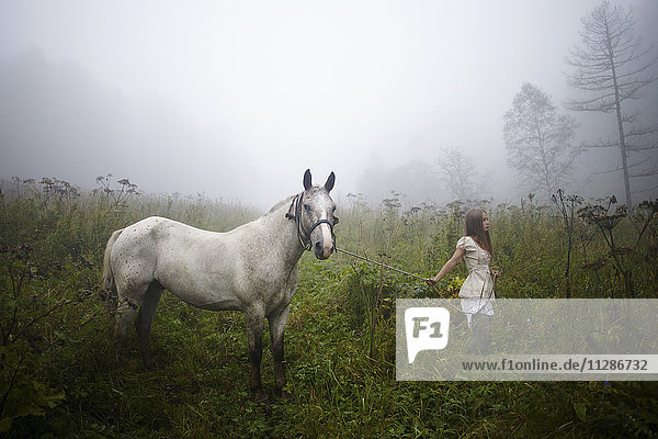 Kaukasisches Mädchen geht mit Pferd im nebligen Feld spazieren