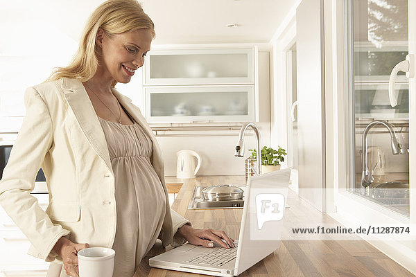 Schwangere Frau benutzt Laptop in der Küche