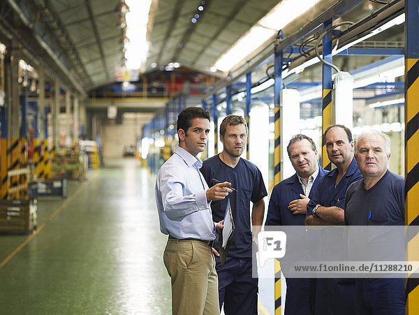 Mann im Gespräch mit Arbeitern in einer Autofabrik