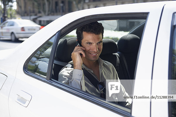Mann auf dem Rücksitz eines Autos  der ein Mobiltelefon benutzt