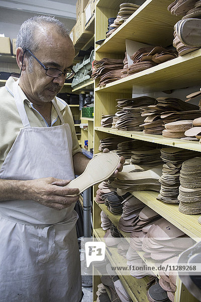 Schuhmacher wählt Schuhsohlen aus einem Regal in seiner Werkstatt aus.