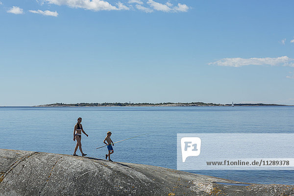 Mother with son walking on rocky coast