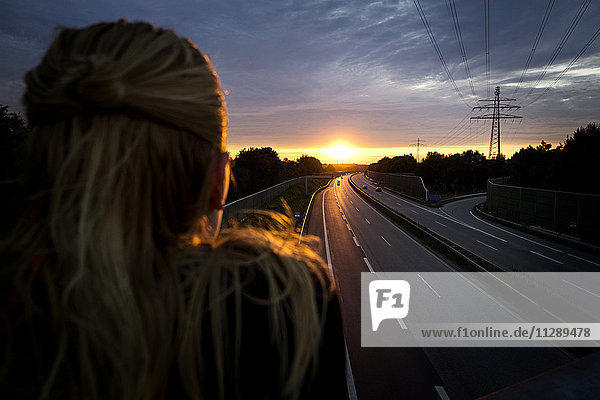Frau bei Sonnenuntergang hinter der Autobahn