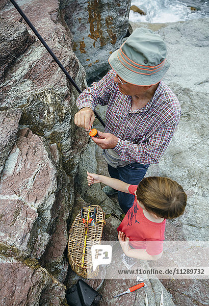 Grandfather teaching grandson fishing at rock coast