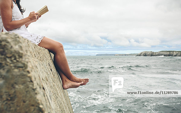 Barefoot woman sitting on pier reading a book  partial view
