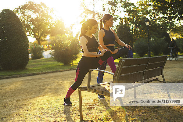 Two young women stretching on park bench at sunset